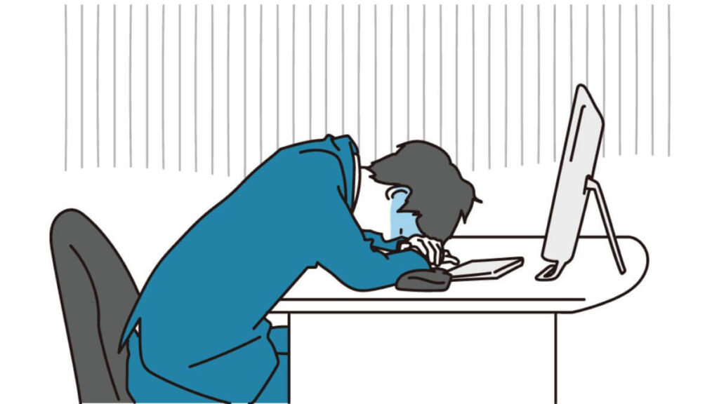 机に頭を置き疲れ果てるスーツ姿の男性