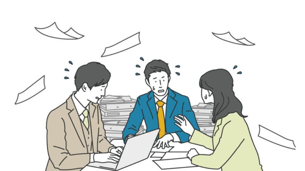 書類の山で忙しく仕事をするスーツ姿の男女3人