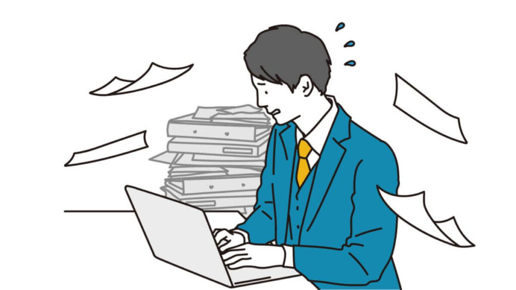 書類の山の中でパソコン作業をするサラリーマン